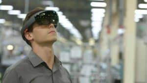 Human male worker is at a manufacturing factory, looking up using augmented reality glasses for quality assurance proposes