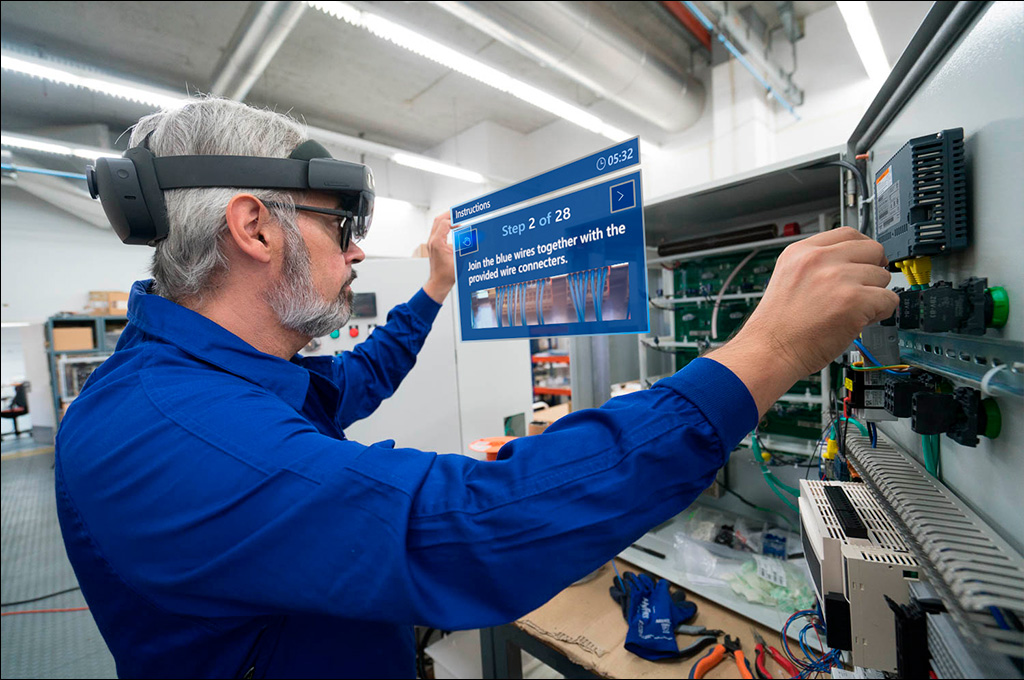 Manufacturing human worker sees the next steps to his task on a blue rectangle that displays augmented reality instructions. It's an augmented worker because he is looking through AR.
